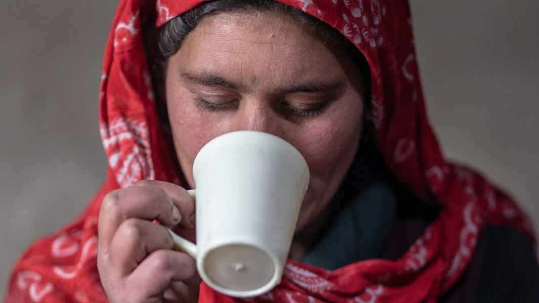 A woman in a red headscarf sips on a cup of tea.