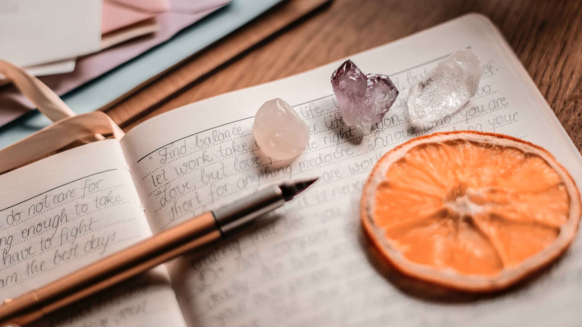a pen, 3 gorgeous crystals and a slice of dried orange are on top of an open journal